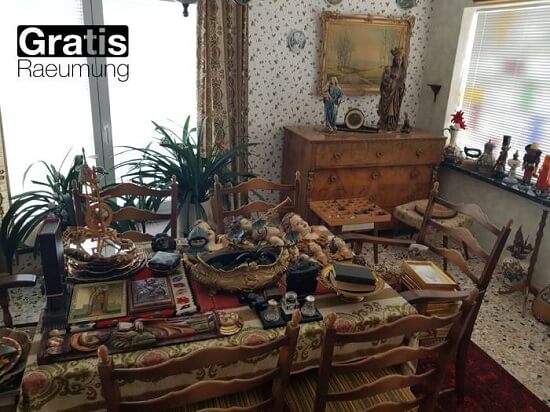 In dem Raum steht ein Tisch, auf dem antike Gegenstände angeordnet sind, um den herum kleine Skulpturen und verschiedene antike Gegenstände stehen.
